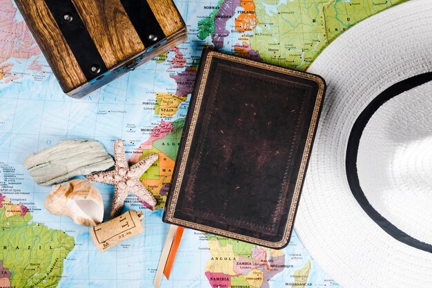Traveler's diary, sea shell and hat on map
