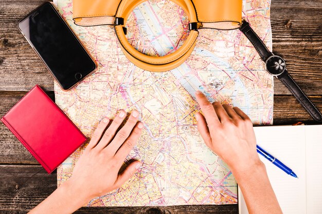 ハンドバッグとスマートフォンで地図上の場所を指す旅行者の手