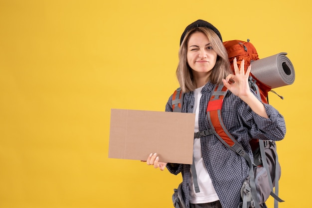 Donna viaggiatrice con zaino in possesso di cartone che fa segno ok