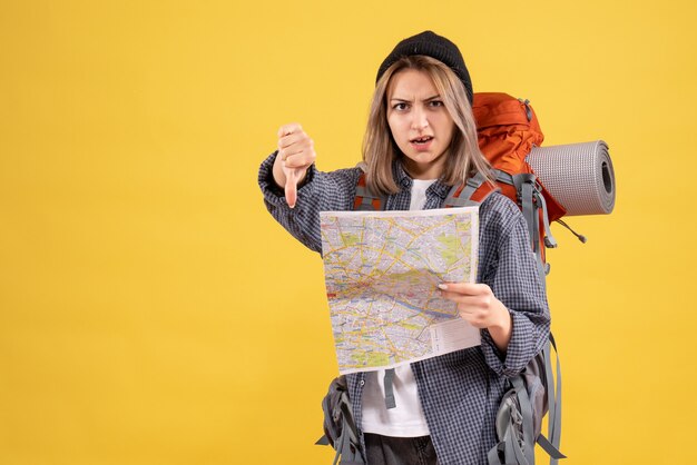 親指を下に与える地図を持ったバックパックを持つ旅行者の女性