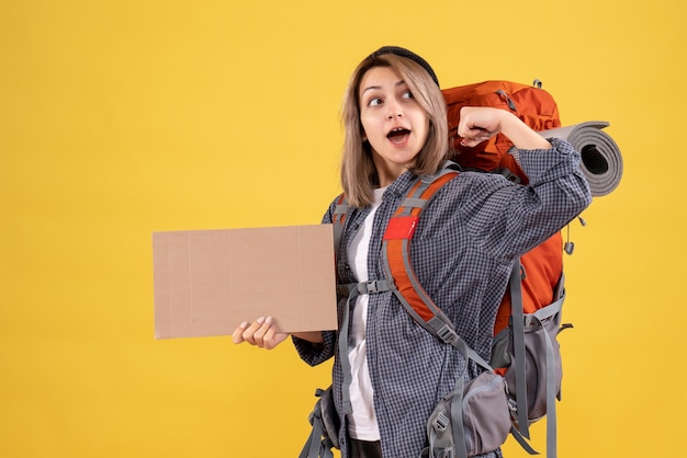 traveler woman with red backpack holding cardboard showing arm muscle