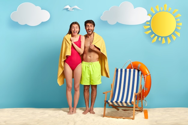 Traveling couple stand together under one towel