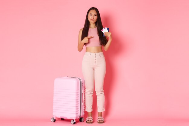 Traveling, holidays and vacation concept. Full-length of disappointed and skeptical asian female tourist in summer clothes complaining over bad airline, pointing at flight tickets and passport