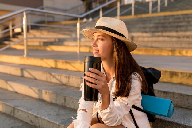 Traveling woman with hat and backpack holding thermos