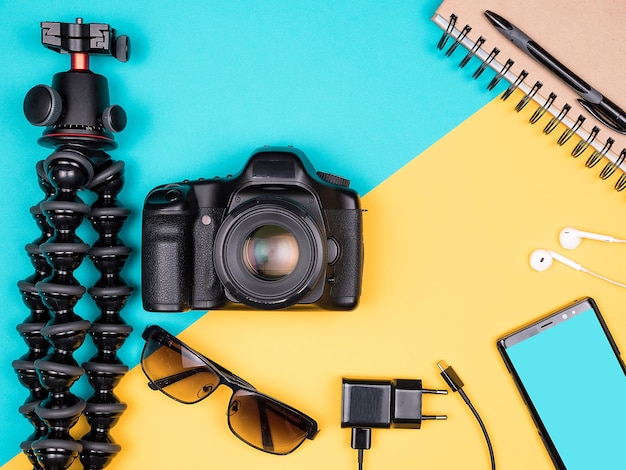 Traveller blogger kit for summer vacation. Top view. Flat lay. Camera with accessories next to sunglasses, paper notebook, smartphone with headset on two colored background. Pastel colors