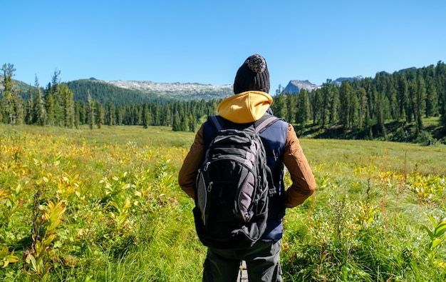 山​を​見ている​バック​パック​を​持つ​旅行者​の​男​。​背面図​。