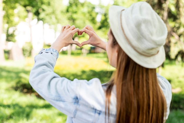 Traveller in the park making a heart shape from behind shot