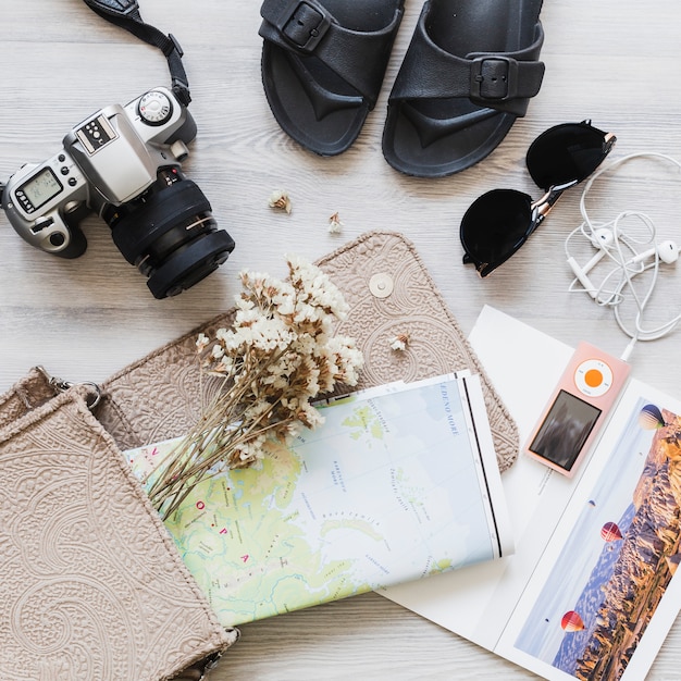 Accessori da viaggio con la mappa e fiore nella borsa sulla scrivania