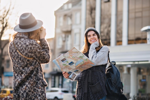 Foto gratuita viaggiare nella soleggiata grande città di ragazze gioiose alla moda. scattare foto, godersi le vacanze, viaggiare con lo zaino, mappa della città. mostrando vere emozioni felici positive, look elegante, in posa per la fotocamera.