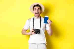 Free photo travelling, vacation and tourism concept. excoted tpirost showing passport with tickets, holding camera and wearing straw hat, standing over yellow background.