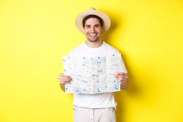 Концепция путешествий, отдыха и туризма. Улыбающийся молодой человек собирается в поездку, держа дорожную карту и улыбается, стоя на желтом фоне.