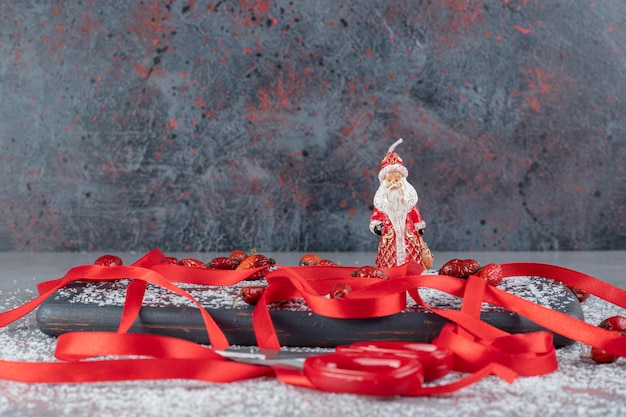 Tray of dog rose fruits, red ribbons, scissors, coconut powder and santa figurine on marble surface