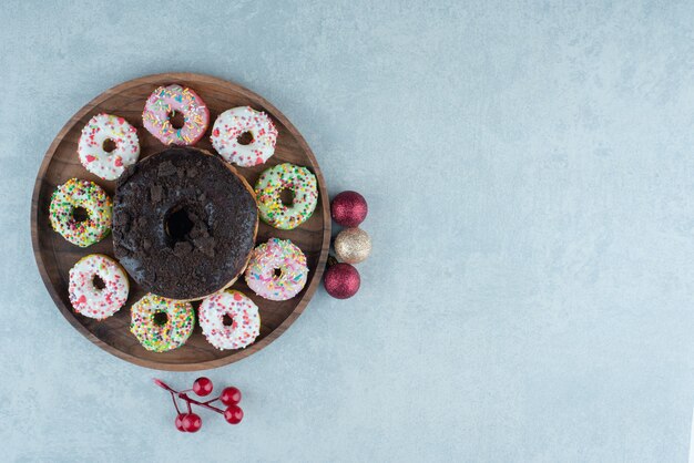 Tray of small donuts around a single, large donut on marble.