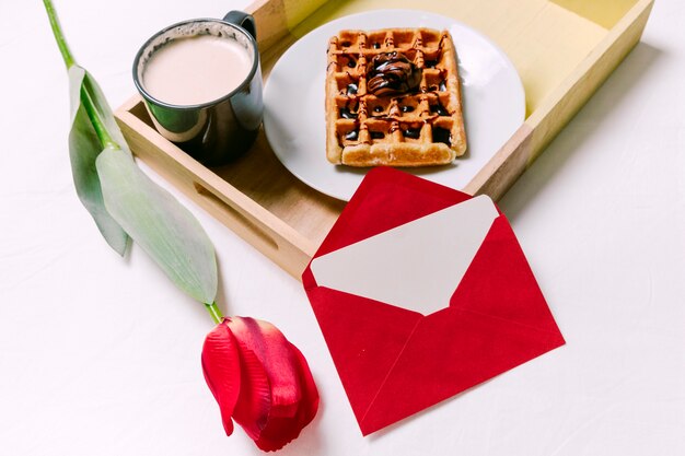 Tray with Belgian waffle and cup of milk on light bed