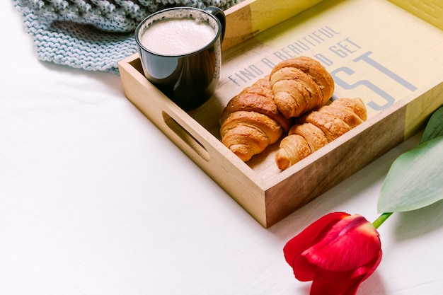Tray with croissants and cup of milk on light bed