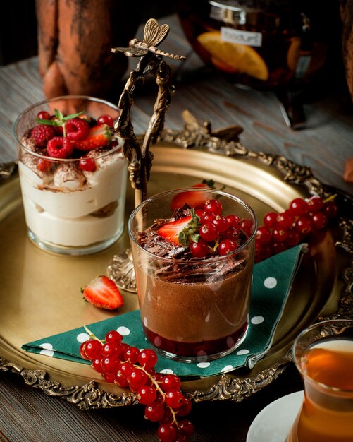 A tray with two glasses of tiramisu and chocolate pudding garnished with berries