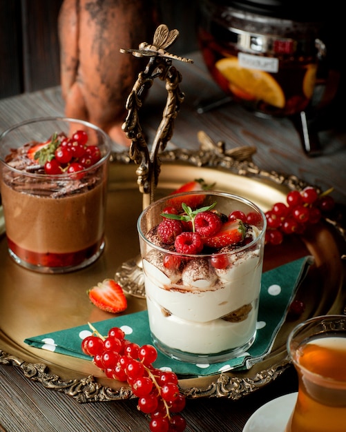 A tray with two glasses of tiramisu and chocolate pudding garnished with berries _