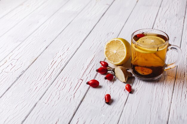 Treating cold. Hot tea with lemon and berries stands on white wooden table