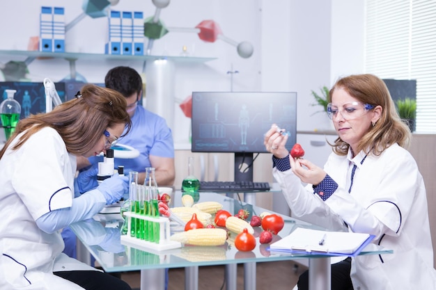 科学者のグループによる実験室での遺伝子操作されたイチゴの治療研究。グリーン溶液で試験管。