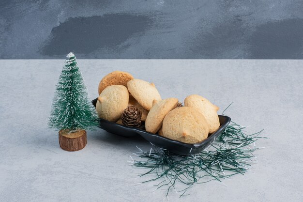 Tree figurine next to a pile of cookeis in a black platter on marble surface