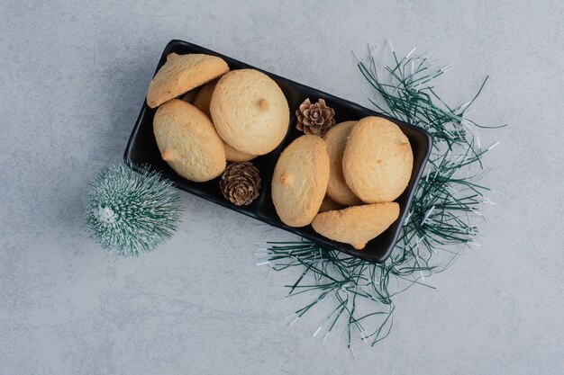 Tree figurine next to a pile of cookeis in a black platter on marble surface