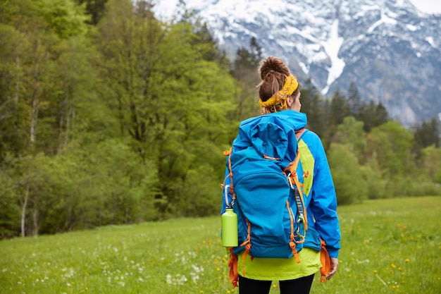 Free photo trekking, wandering and hiking concept. active woman hiker poses on hilltop, strolls against mountain landscape, has active rest