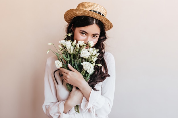 꽃을 스니핑 유행 아시아 여자. 흰색 eustomas의 꽃다발을 들고 로맨틱 갈색 머리 젊은 여자.