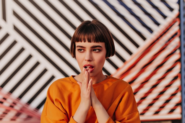 Trendy brunette woman in orange stylish sweatshirt looking away in cafe