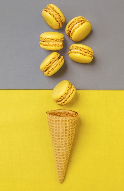 Free photo trendy color of the year 2021. illuminating yellow and ultimate gray. yellow macaroons and an sugar cone on gray wall, flat lay.
