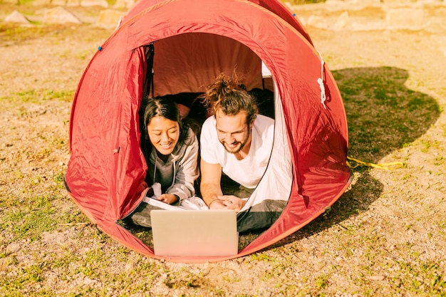 Trendy couple lying in tent with laptop