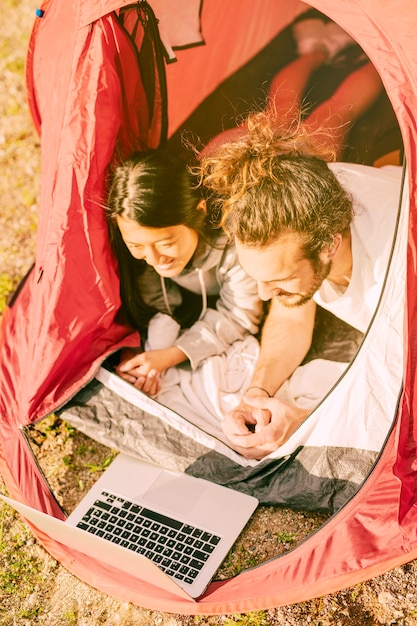 Coppie alla moda che si rilassano in tenda con il computer portatile