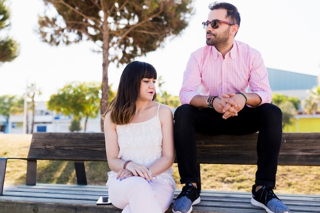 Trendy couple sitting on wooden bench at outdoors