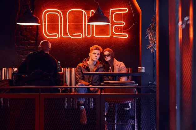 Trendy dressed young stylish couple sitting in a cafe with industrial interior