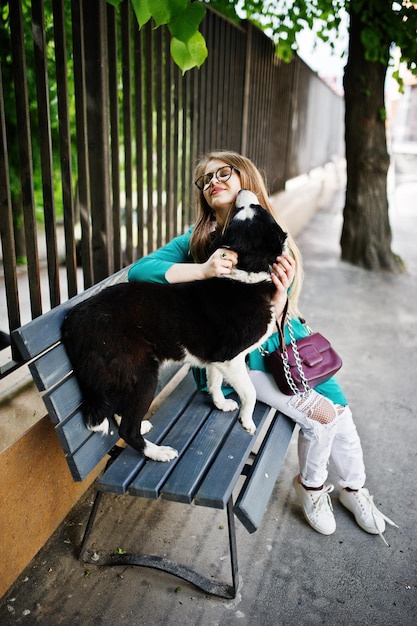Foto gratuita ragazza alla moda con occhiali e jeans strappati con cane husky russoeuropeo laika al guinzaglio contro una panchina sulla strada della città amico umano con tema animale