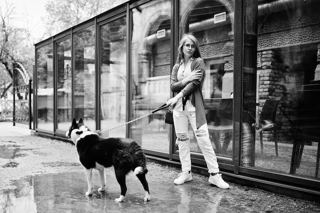 Trendy girl at glasses and ripped jeans with russoeuropean laika husky dog on a leash against street of city Friend human with animal theme