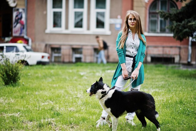 안경을 쓴 트렌디한 소녀와 러시아인 라이카 허스키 개가 도시의 거리에 가죽끈으로 묶인 찢어진 청바지 동물 테마를 가진 친구 인간