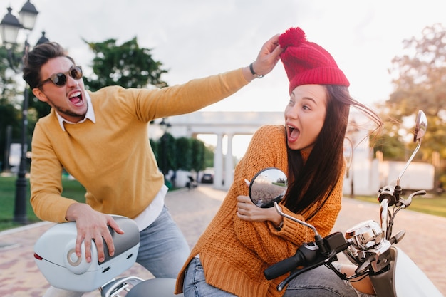 Trendy guy with beard joking with friend holding her red hat