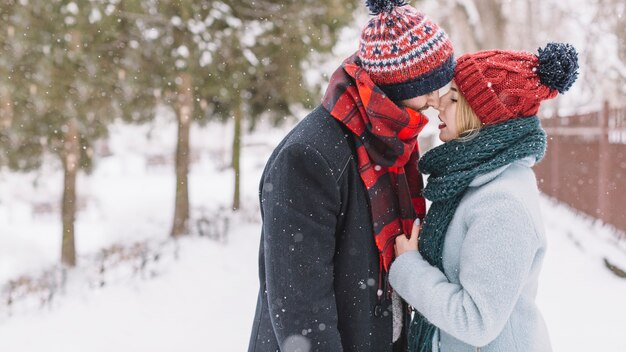 Trendy loving couple kissing in snowfall