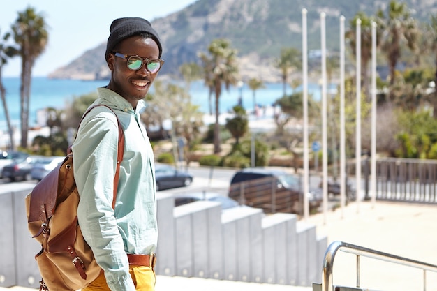 Модный студент в шляпе и очках, наслаждаясь солнечной теплой погодой