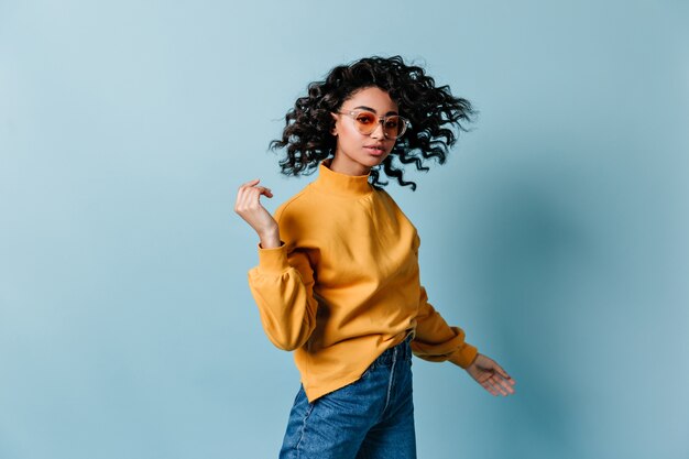 Trendy young woman dancing on blue wall