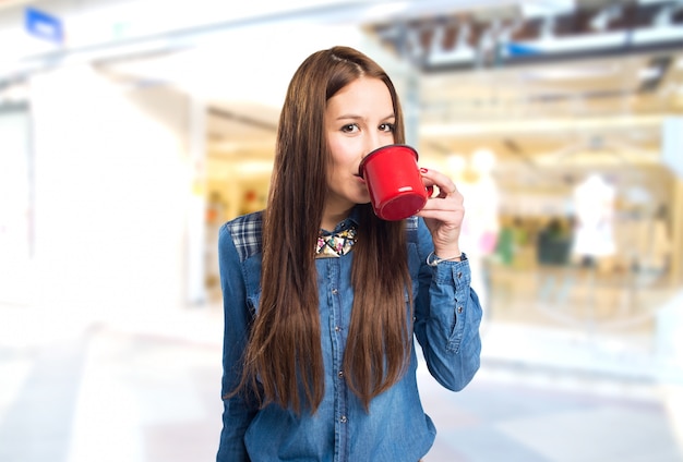 Moda giovane donna che beve da una tazza rossa