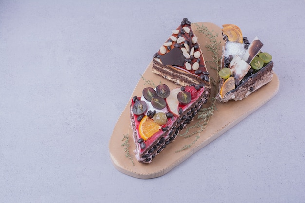 Triangle cake slices with chocolate and fruits on a wooden board