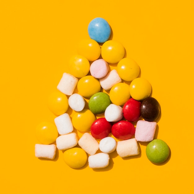 Free photo triangle candies with white marshmallows on yellow backdrop