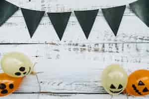 Free photo triangle dark flags hanging above and balloons with creepy faces below on wooden background