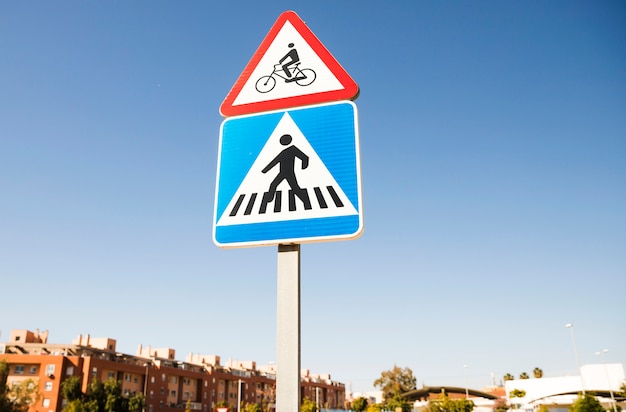 Triangular bicycle warning sign over the square pedestrian crossing road sign in the city