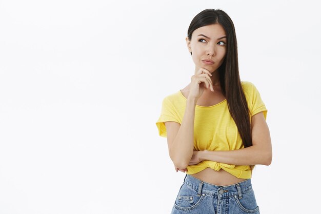 Tricky and smart creative young stylish female in yellow girlfriend planning how to get revenge squinting lifting eyebrow while thinking