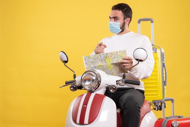 黄色いスーツケースを乗せたバイクに医療マスクを着た自信のある男と、黄色を前に向けた地図を持った旅行のコンセプト