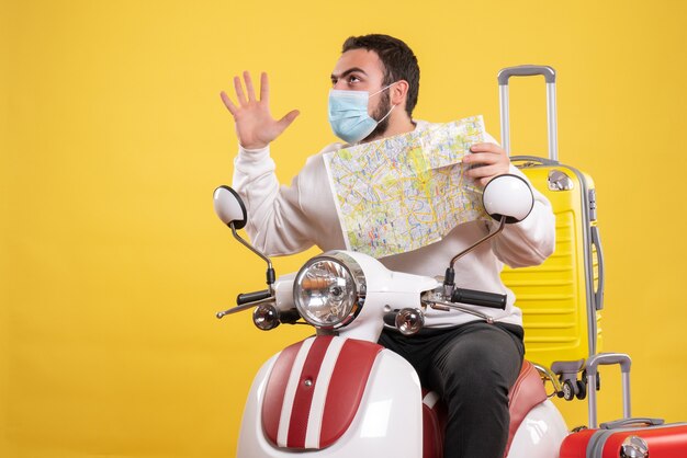 Trip concept with confident guy in medical mask sitting on motorcycle with yellow suitcase on it