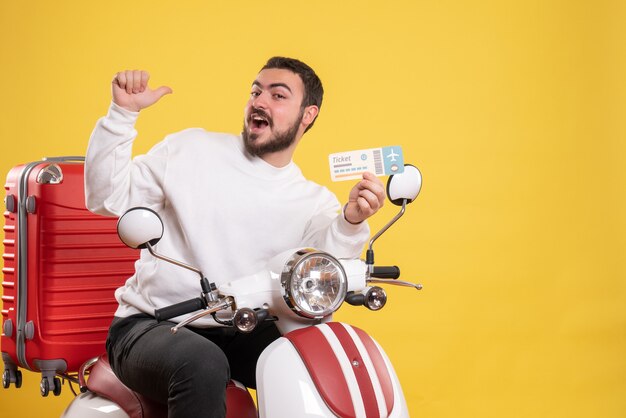 Trip concept with smiling man sitting on motorcycle with suitcase on it showing ticket on yellow