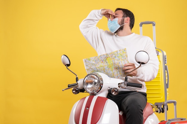 노란색 가방에 오토바이에 앉아 나쁜 냄새 제스처를 만드는지도를 들고 의료 마스크에 젊은 남자와 여행 개념